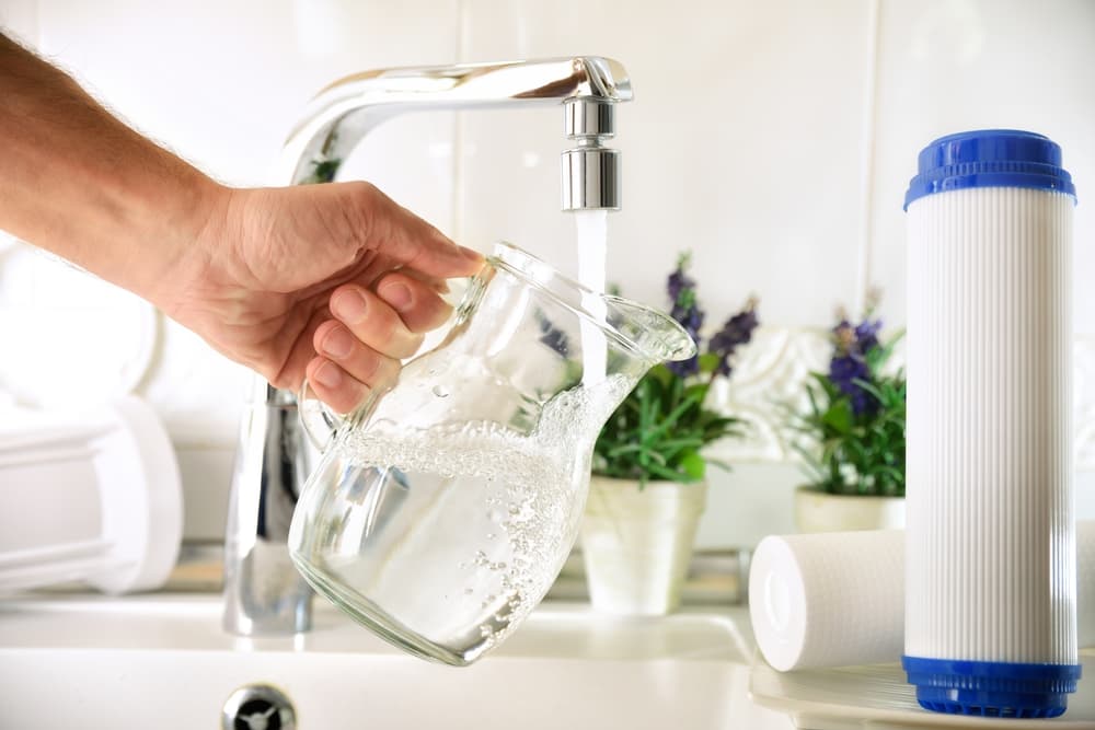 man pouring tab water on a jug next to RO system filters